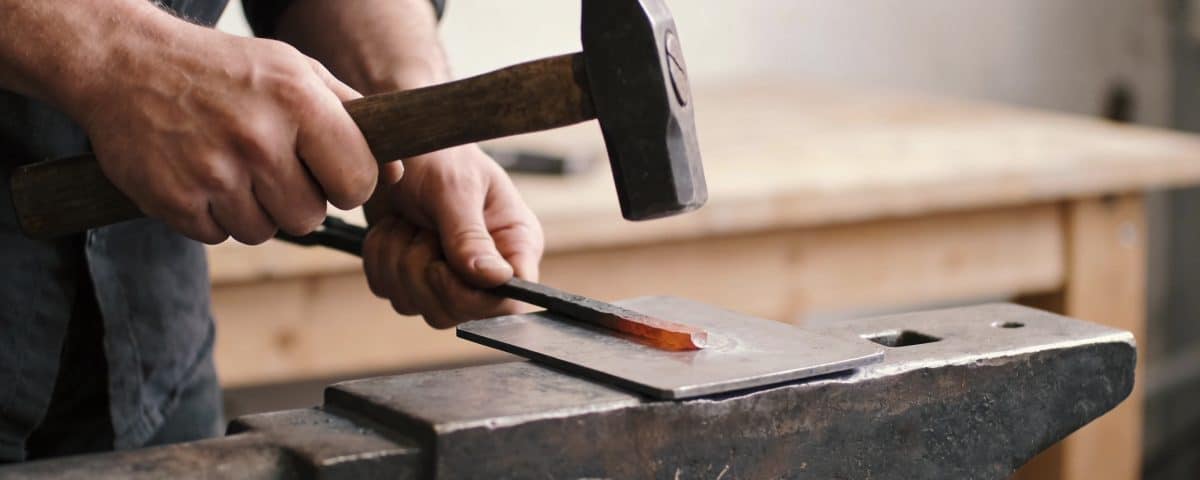 artisan martelant une plaque de metal sur enclume
