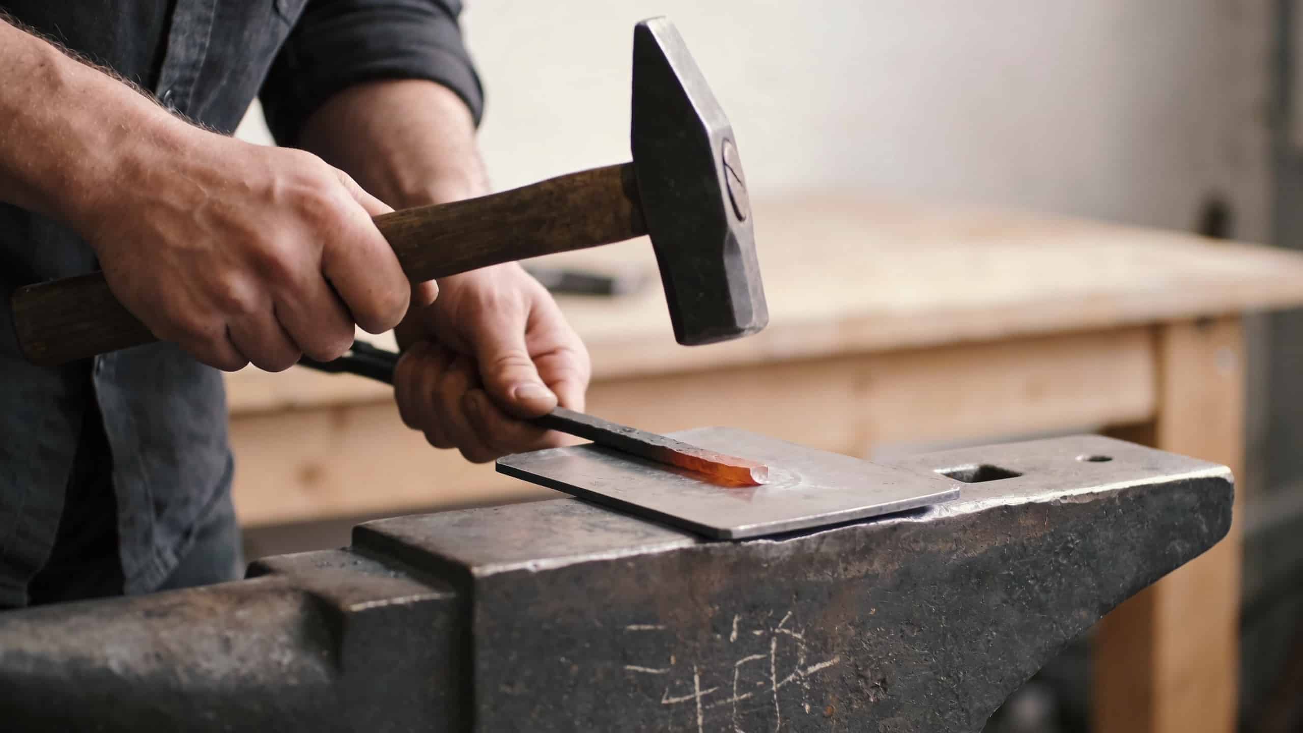 artisan martelant une plaque de metal sur enclume