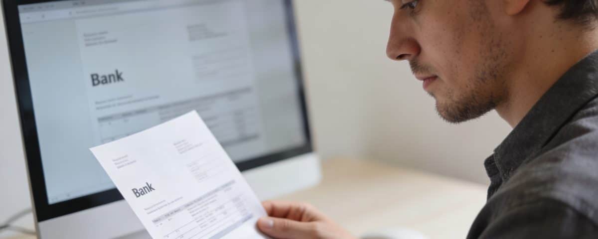 client regarde relevé bancaire devant écran ordinateur