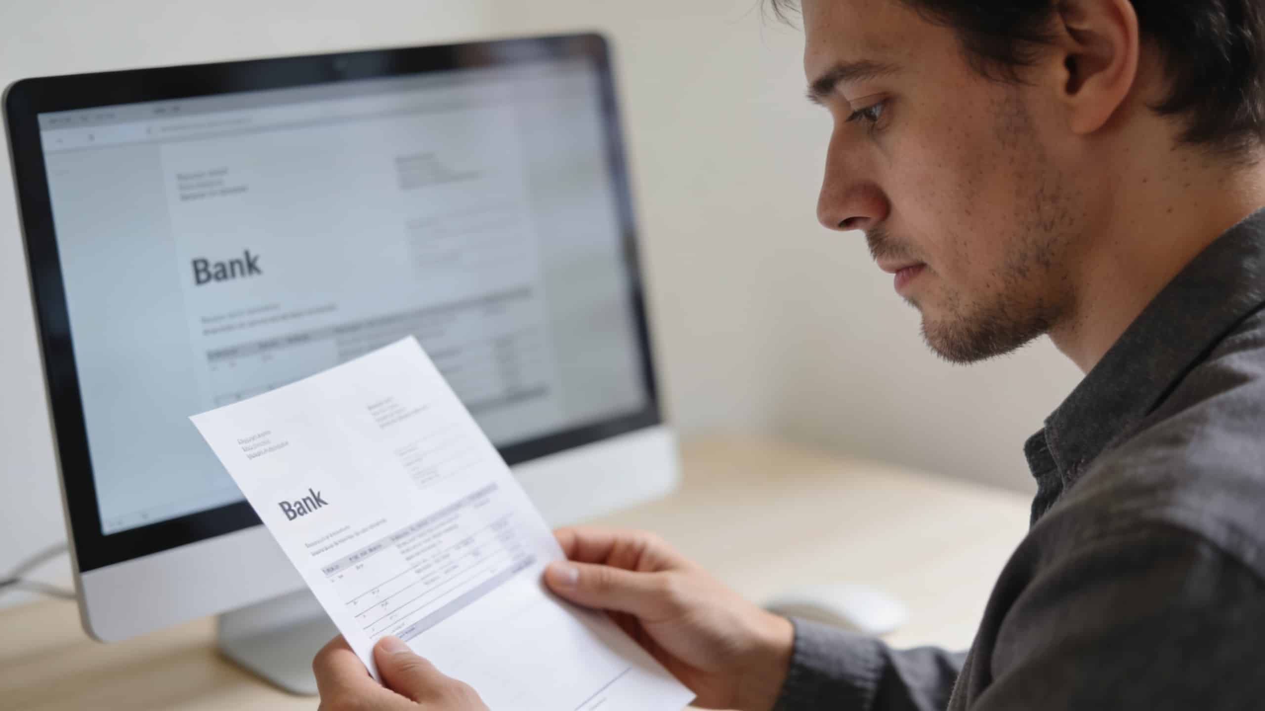 client regarde relevé bancaire devant écran ordinateur