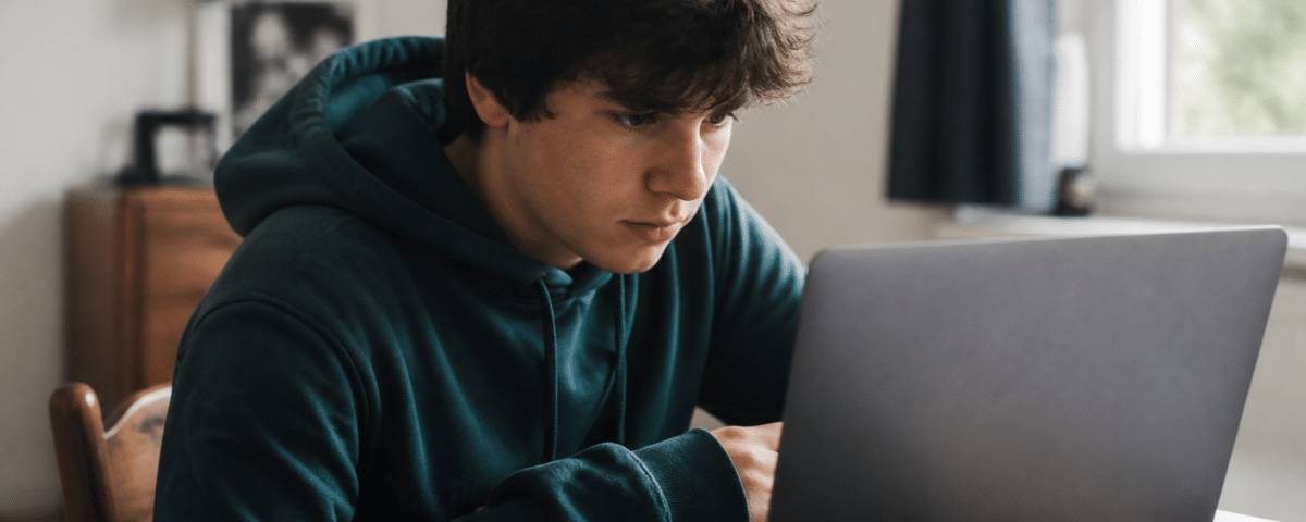Adolescent assis a un bureau consultant son ordinateur portable