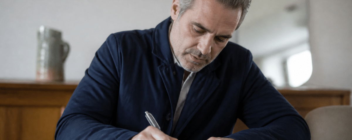 Homme d'age moyen signant un document officiel assis.