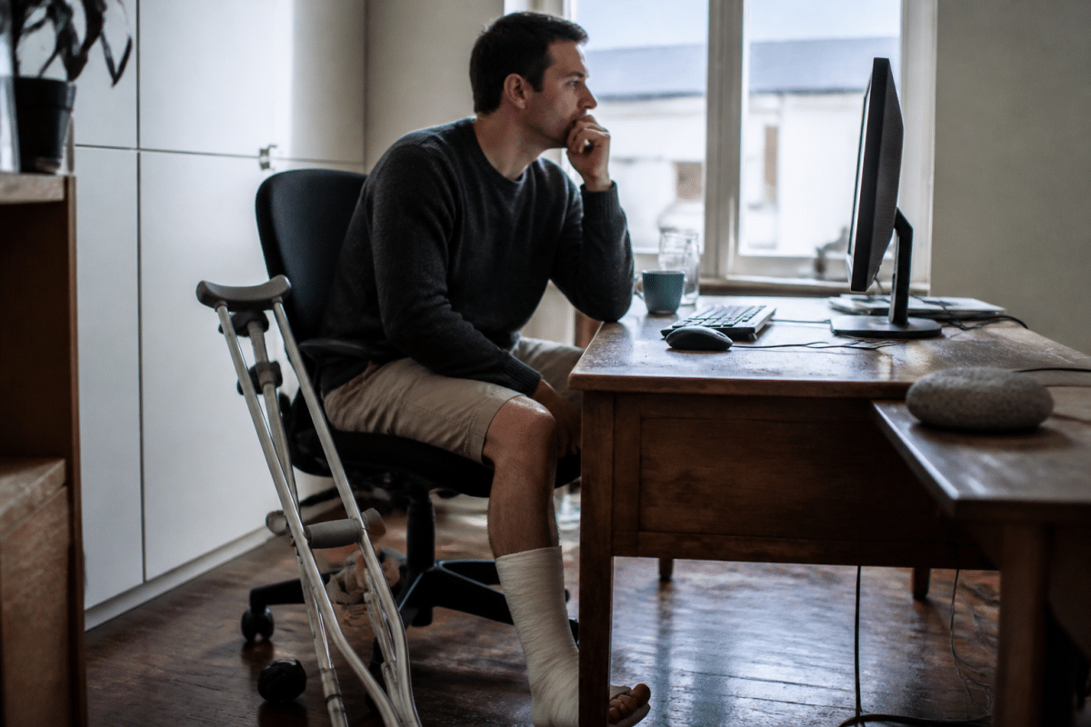 Patient avec bequilles assis au bureau apres chirurgie