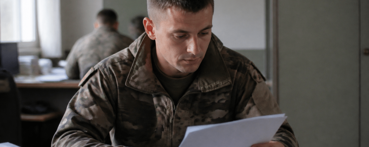 Soldat en uniforme consulte document militaire assis bureau.
