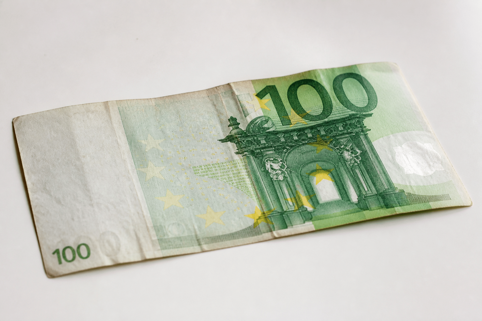 Vieux billet cent euros posé sur surface blanche.