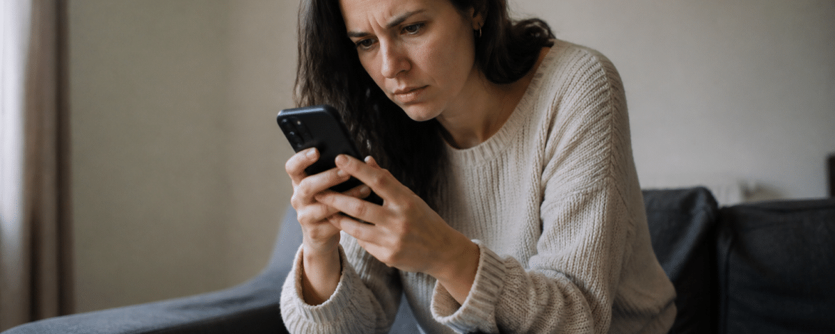 Femme assise regardant son telephone avec expression confuse.